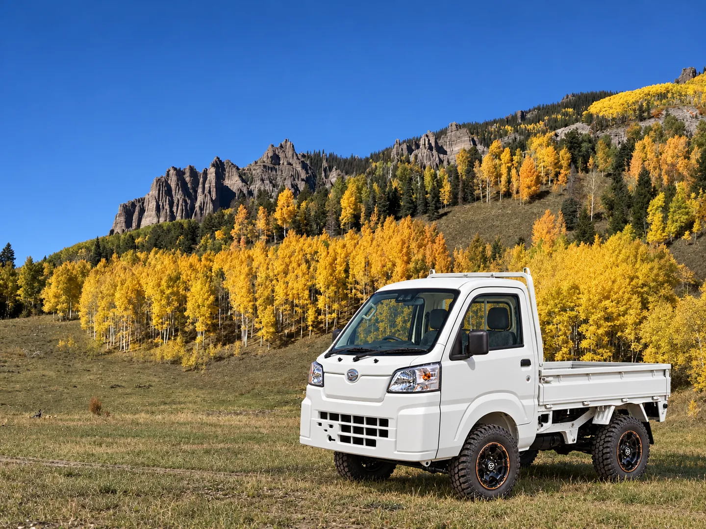 A white Hijet mini truck in an autumn meadow below a rocky ridge and golden aspens